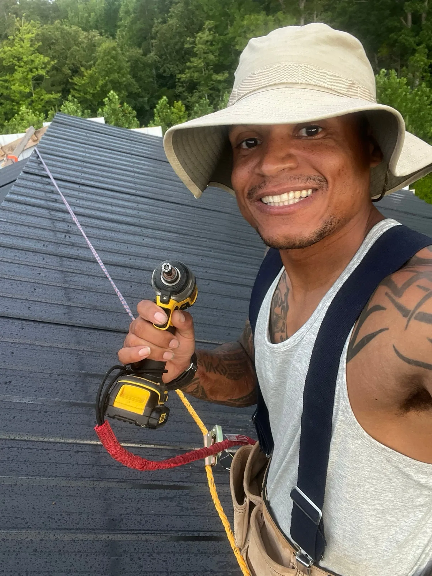 Josh smiling on the metal roof of a new building with a drill in hand