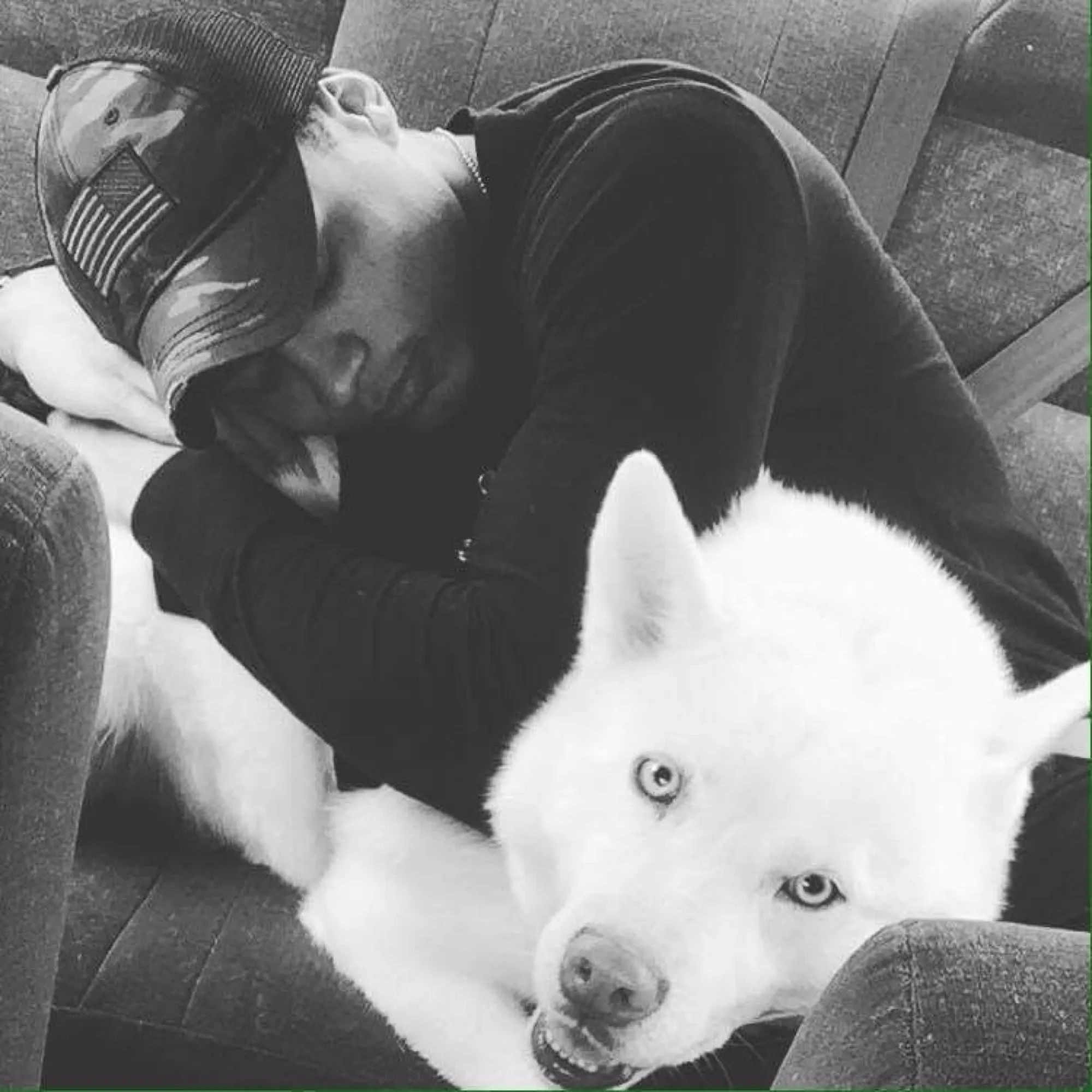 A man resting his head beside a white husky on the couch, both at ease